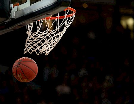 A basketball is about to go through the hoop, surrounded by a net, with a crowd blurred in the background.