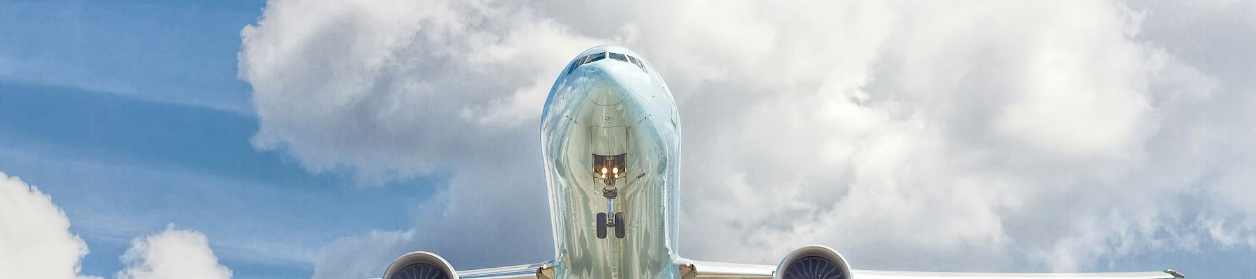 An airplane captured mid-flight, viewed from underneath against a backdrop of a partly cloudy blue sky.