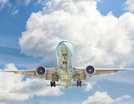 An airplane captured mid-flight, viewed from underneath against a backdrop of a partly cloudy blue sky.