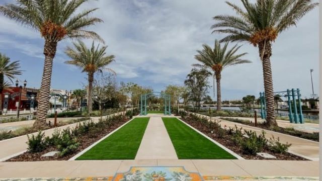 A landscaped pathway lined with palm trees leads to a garden archway, featuring a decorative tile design in the foreground.