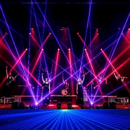 A vibrant stage performance with musicians, drummers, and colorful laser lights creating dynamic patterns in a lively atmosphere.