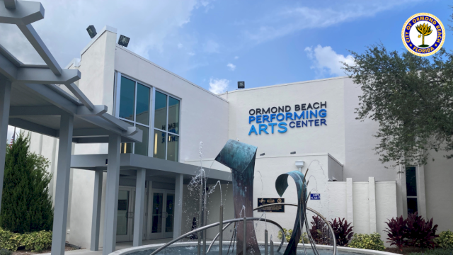 The image shows the Ormond Beach Performing Arts Center with a modern sculpture and fountain in front, under a partly cloudy sky.