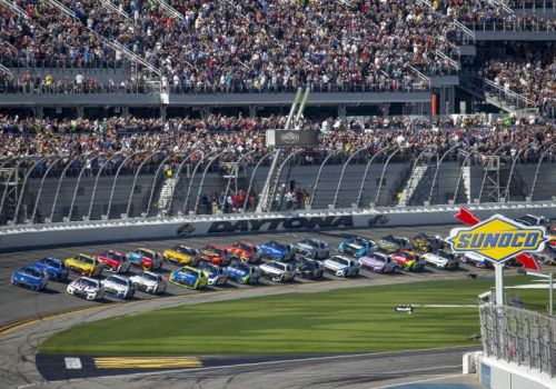 Daytona racetrack crowded with NASCAR stock cars lined up near a Sunoco logo, with packed grandstands behind them.