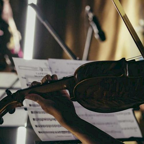 A person is playing a violin in front of sheet music, with dim lighting and a microphone stand in the background.