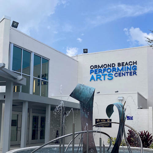The image shows the Ormond Beach Performing Arts Center with a modern sculpture fountain in front and a logo on the building.
