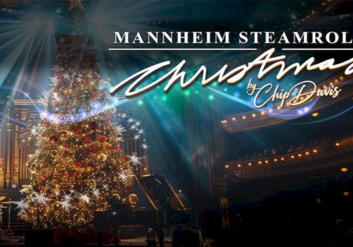 A festive stage with a lit Christmas tree, sparkling lights, and &ldquo;Mannheim Steamroller Christmas by Chip Davis&rdquo; signage glowing in the background.