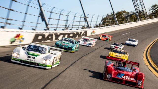 The image shows a group of race cars on a track with "Daytona" written on a wall, racing around a curve in a competitive event.