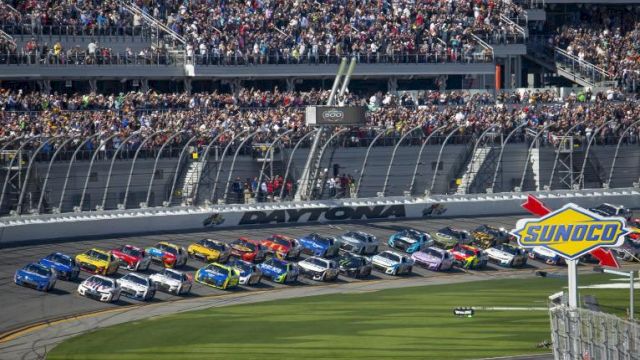 A group of race cars on a track, with a large crowd of spectators and a "Sunoco" sign visible, at a motorsport event.