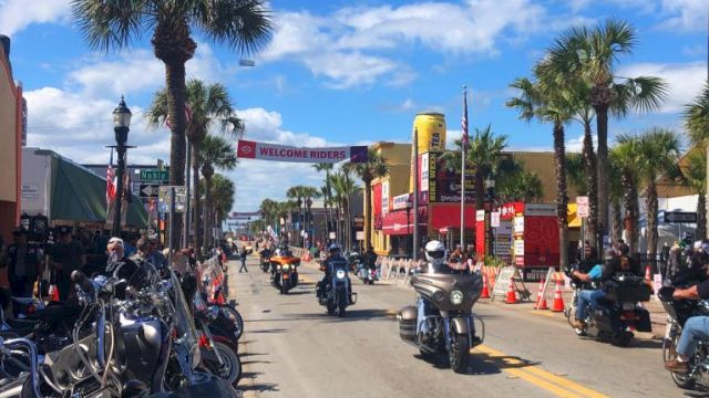 A street scene with motorcycles, palm trees, and a "Welcome Riders" banner, suggesting a motorcycle event or rally.