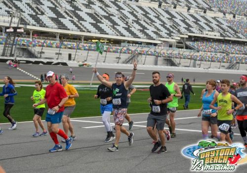 Runners celebrate at the Daytona Beach 12 Marathon inside a packed stadium, raising arms as they finish the race.