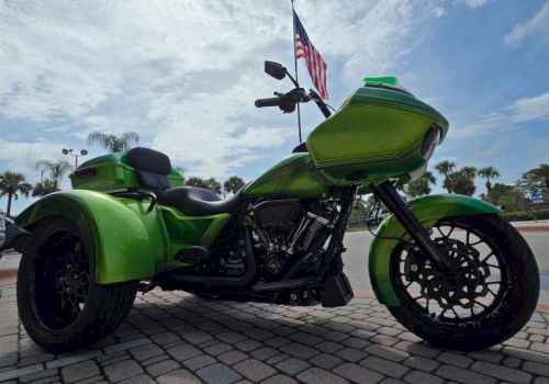 Green motorcycle parked outside near an American flag on a cloudy day.