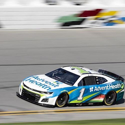 A race car with "AdventHealth" branding speeds on a track, featuring blue, green, and white colors.