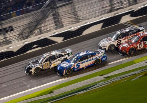 Several race cars are competing on a track, closely packed together, with a blurred background indicating high speed action.