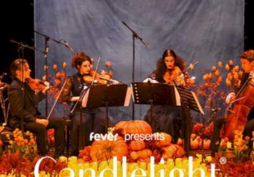 A string quartet performs on stage surrounded by pumpkins and autumn decor, under the banner "fever presents Candlelight."