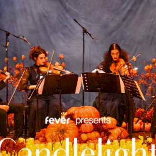 A string quartet performs on stage surrounded by pumpkins and autumn decor, under the banner "fever presents Candlelight."