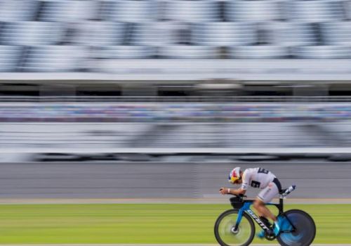 A cyclist in motion on an aerodynamic bike, racing against a blurred background on a track.