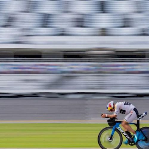 A cyclist in motion on an aerodynamic bike, racing against a blurred background on a track.
