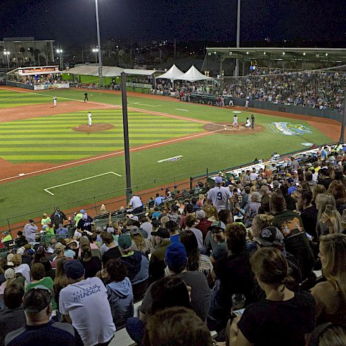 A nighttime baseball game with a crowded stadium, bright lights illuminating the field, and people watching from the stands.