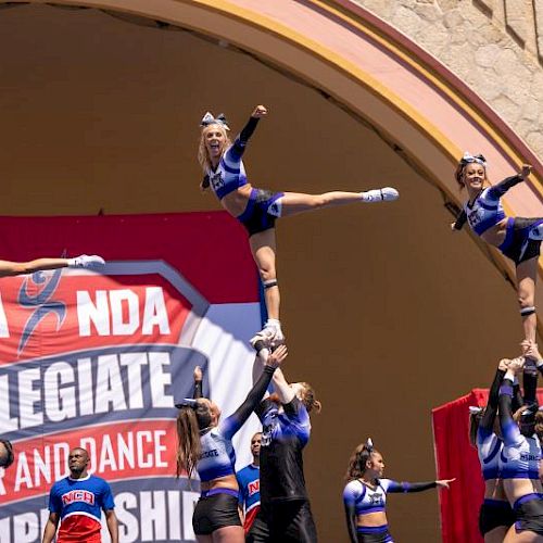 Cheerleaders performing stunts at the NCA & NDA Collegiate Cheer and Dance Championship in front of a banner.