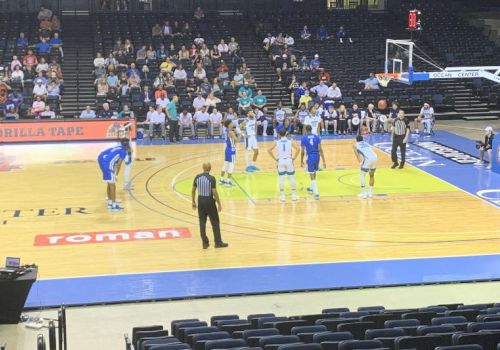 A live basketball game in an arena with players on the court and fans in the stands, near the hoop and free-throw area.