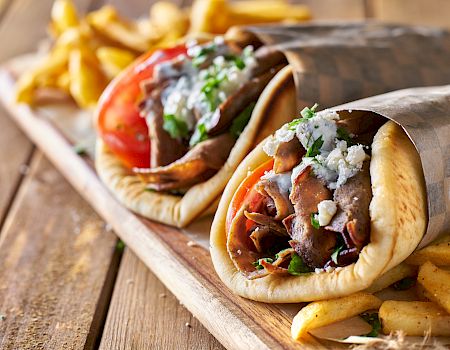 Two wraps filled with meat, tomatoes, herbs, and sauce, served with fries on a wooden board.