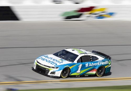 A blue-and-white race car with number 1 speeds on a track during a motorsport race, with a blurred background.