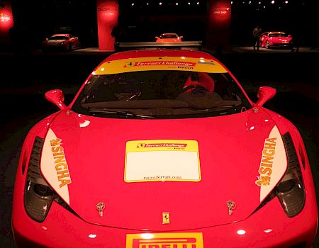 A red Ferrari race car with Pirelli logo, sponsor decals, yellow license area, and showroom lighting in the background.