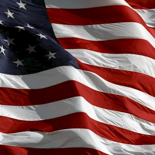 A waving American flag with red and white stripes and a blue canton of stars, fluttering in the wind.