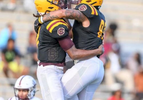 Two football players in yellow-and-black uniforms embrace in a tight celebratory hug on the field.