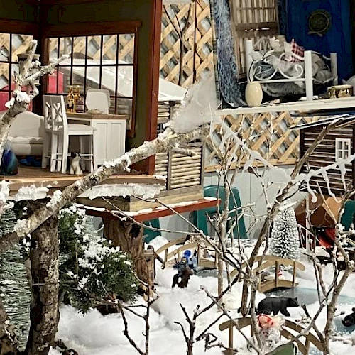 A cozy, snow-dusted outdoor seating area with a mix of vintage furniture and string lights, tucked beside a colorful cabin.