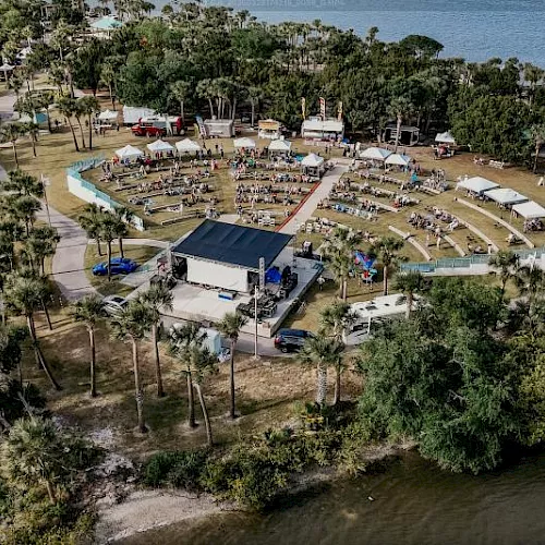 Aerial view of a large outdoor event setup with many chairs and tables on a waterfront property near the beach.