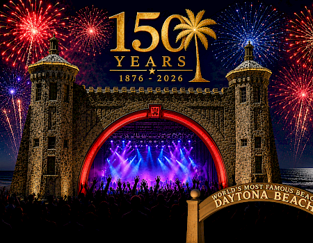 “56 years” themed fireworks over a beach concert stage with a glowing purple show beneath two stone towers.