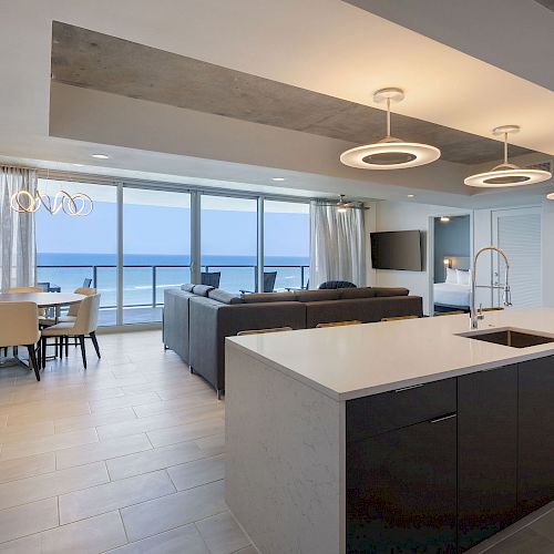 A modern, open-concept living space with a kitchen island, dining area, and seating area, featuring large windows with an ocean view.